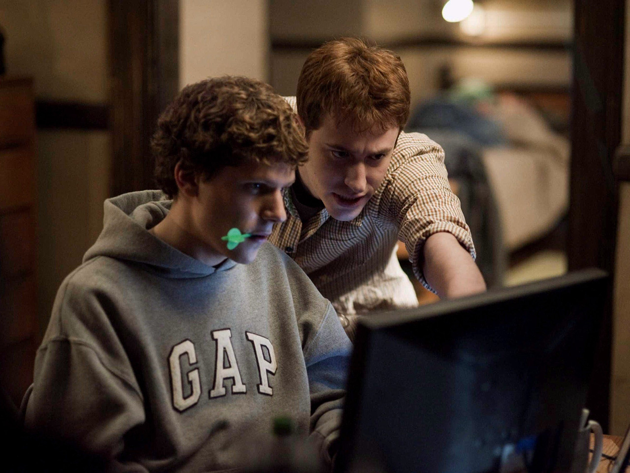 Mark Zuckerberg starrt in seinen Laptop und kaut dabei auf einem grünen Dartpfeil